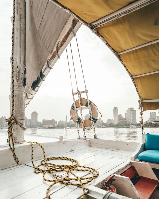 View from the deck of a boat with a lifebuoy and coiled rope, looking out at a city skyline across the water.