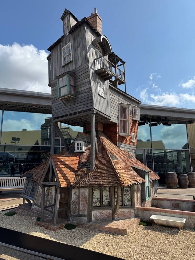 Una casa sbilenca a più piani, in legno e mattoni, con un tetto di tegole, si erge in un cortile sotto un cielo blu.