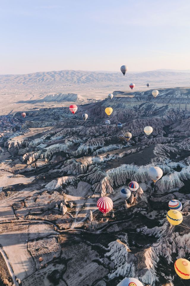 An aerial view of colorful hot air balloons floating over a vast landscape of rocky valleys at sunrise.