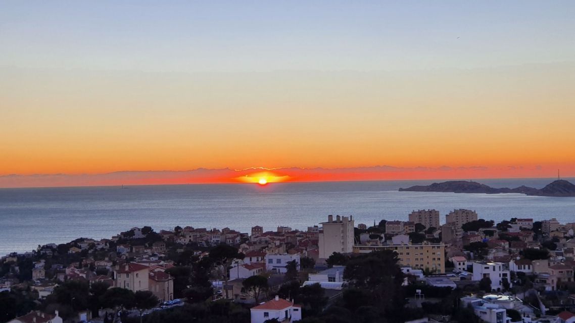 Le soleil se couche sur l'horizon au-dessus de la mer, illuminant une ville côtière de sa lueur orangée.