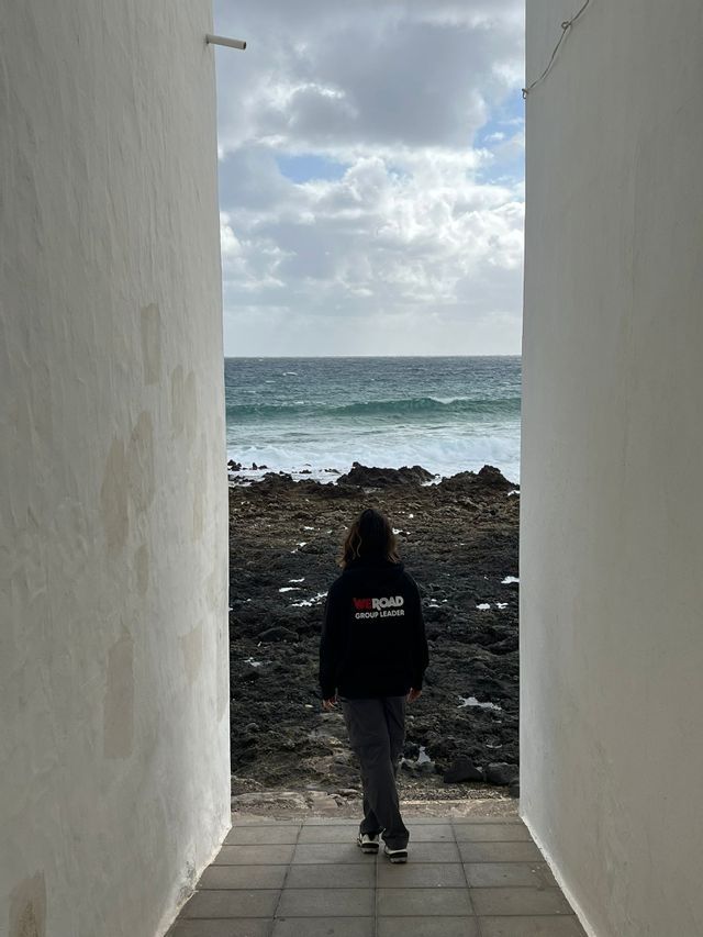 Una persona di spalle, con indosso una felpa da Group Leader WeRoad, cammina lungo uno stretto passaggio verso una costa rocciosa.