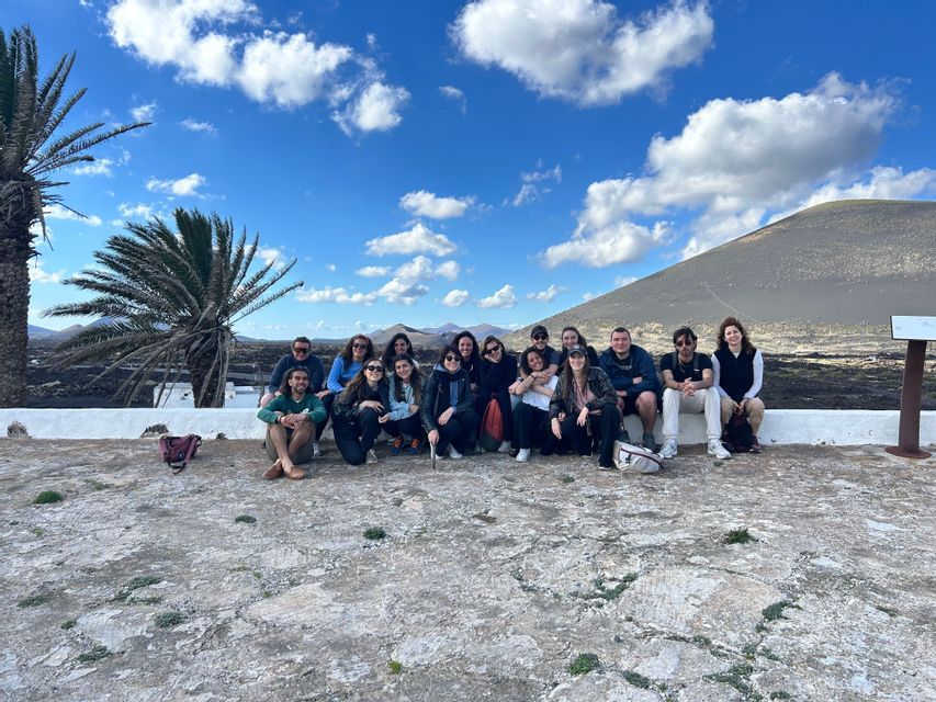 Un viaje en grupo de WeRoad posa para una foto en un mirador de piedra con una colina volcánica y palmeras de fondo.
