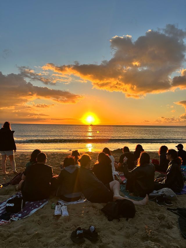 Un viaggio di gruppo WeRoad seduti su una spiaggia sabbiosa ad ammirare il tramonto dorato sull'oceano.