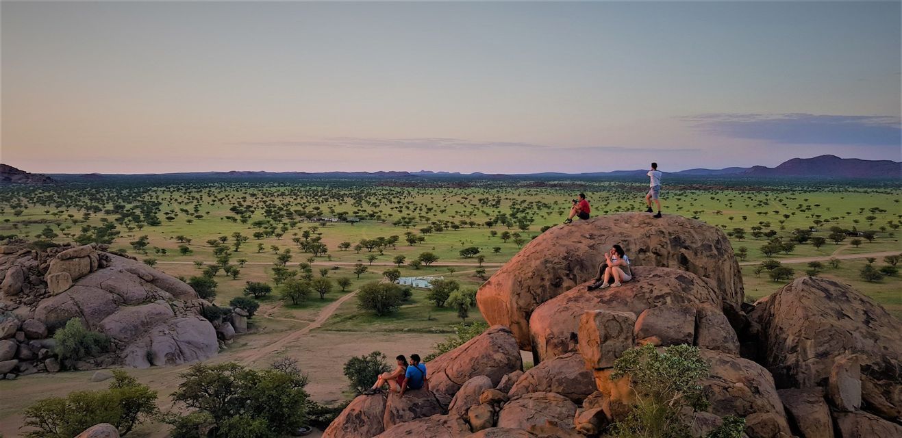 Viaggio di gruppo WeRoad per ammirare il tramonto da grandi massi con vista su una vasta savana punteggiata di alberi.
