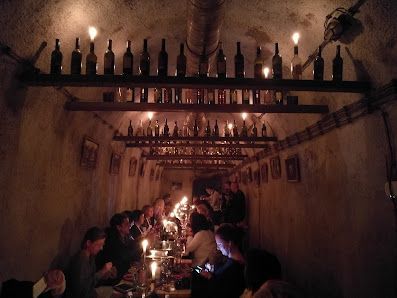 Un grupo de WeRoad cena en una bodega rústica e iluminada con velas, con botellas de vino dispuestas en estantes.