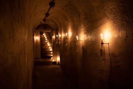 Velas en botellas de vidrio montadas en la pared iluminan un oscuro túnel de piedra arqueado que lleva a una escalera.