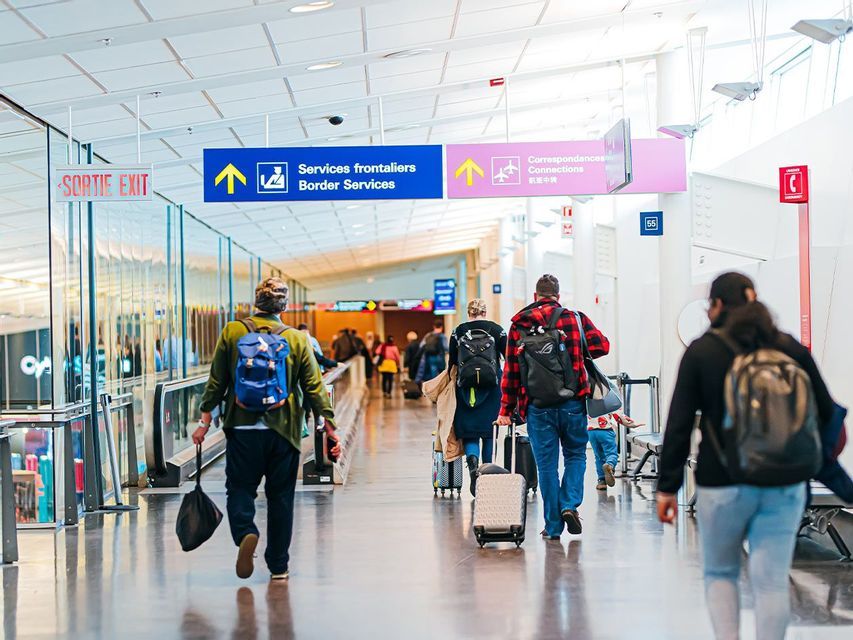 Un groupe WeRoad de voyageurs avec sacs à dos et bagages traversant un terminal d'aéroport lumineux, suivant les panneaux.