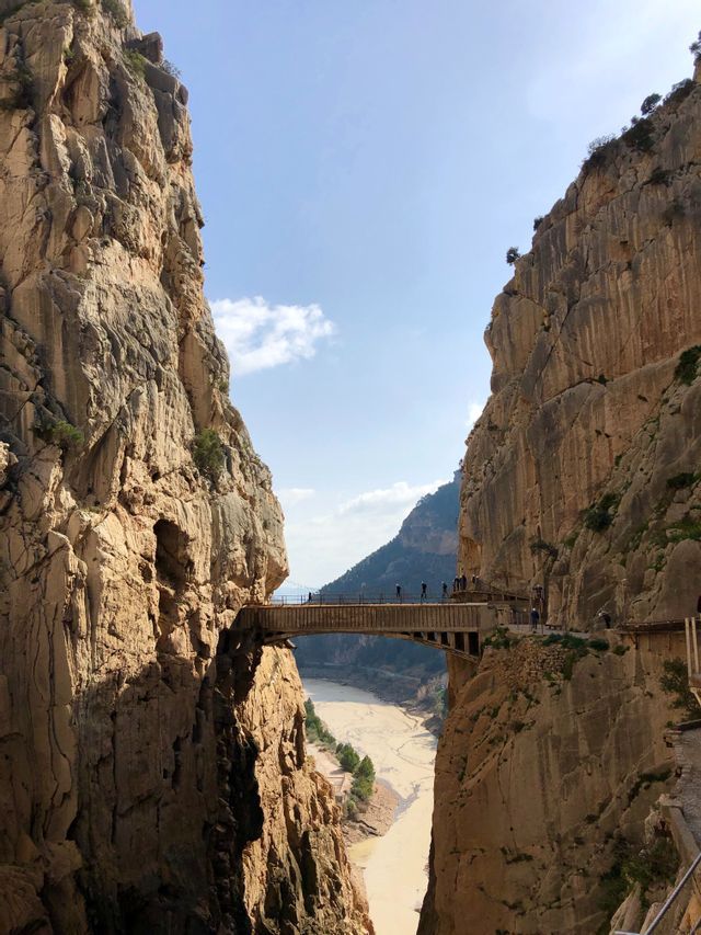 Un gruppo WeRoad percorre uno stretto ponte aggrappato alle ripide pareti di un profondo canyon, con un fiume fangoso che scorre sotto.