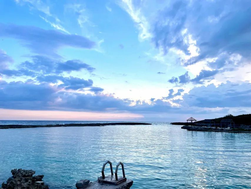 Una escalera metálica en un muelle rocoso que lleva a una ensenada tranquila bajo un cielo nublado al atardecer.