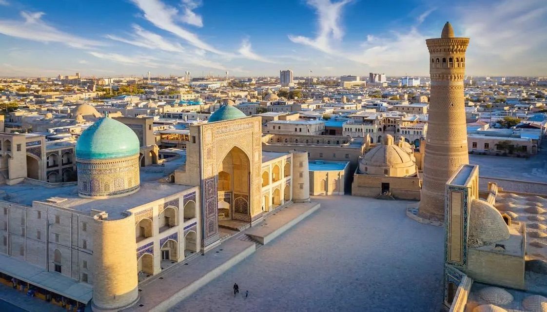 Vue aérienne d'une place historique avec un dôme turquoise et un haut minaret au lever du soleil.