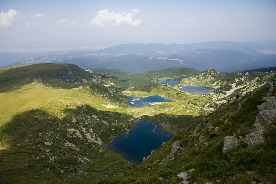 Vue aérienne d'une vallée de montagne verdoyante et luxuriante, parsemée de plusieurs lacs alpins d'un bleu profond.
