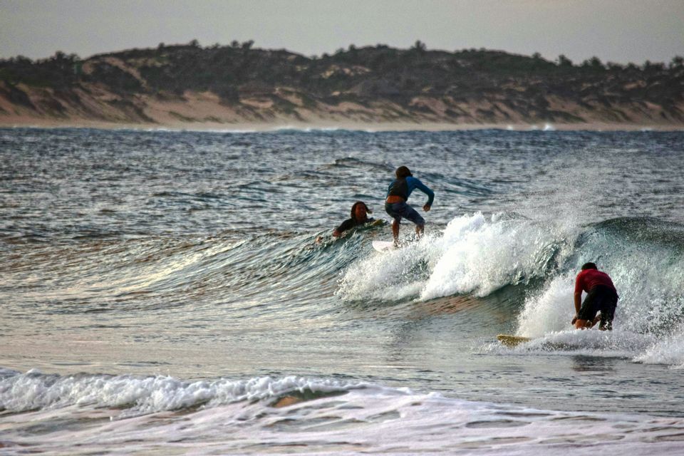 Three surfers riding waves in the ocean with a distant hilly shoreline in the background.