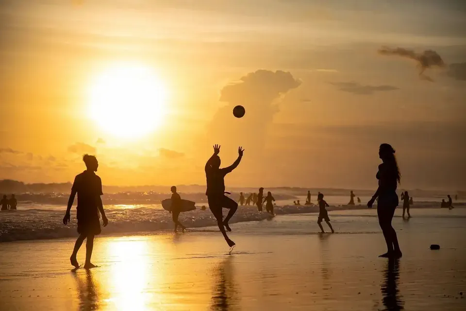 Silhouettes of a WeRoad group trip playing with a ball on a beach during a golden sunset, with reflections on the wet sand.
