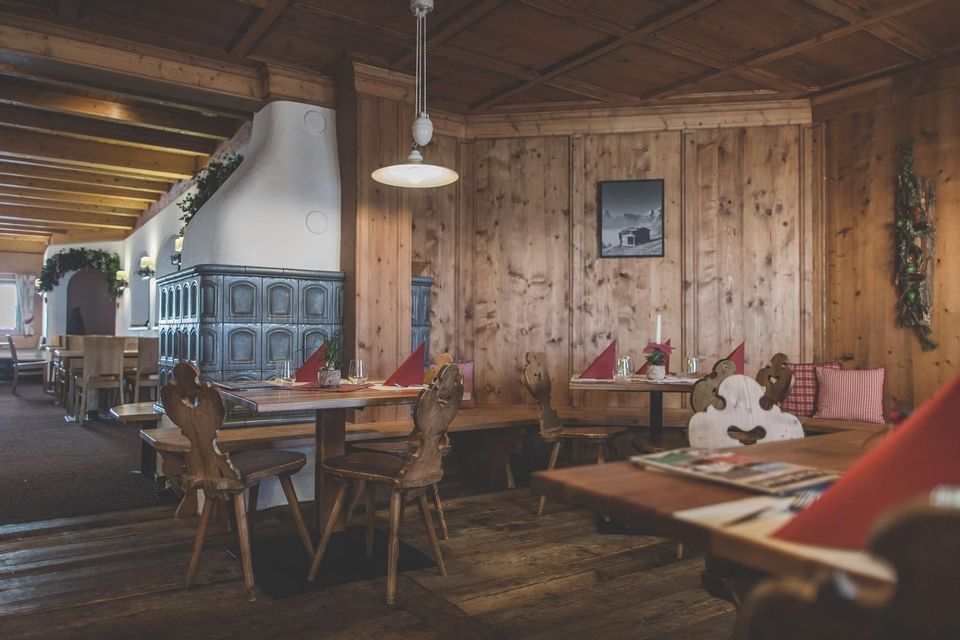 The rustic wooden interior of a restaurant with set tables, carved chairs, and a traditional tiled stove.