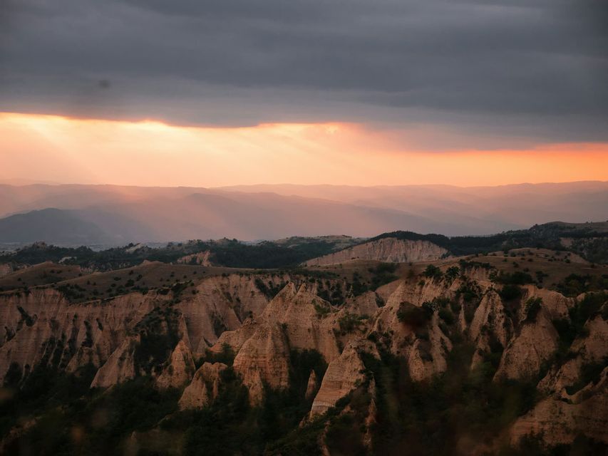 Au coucher du soleil, des rayons de soleil percent les nuages sombres, éclairant un vaste paysage de formations rocheuses érodées et pointues.
