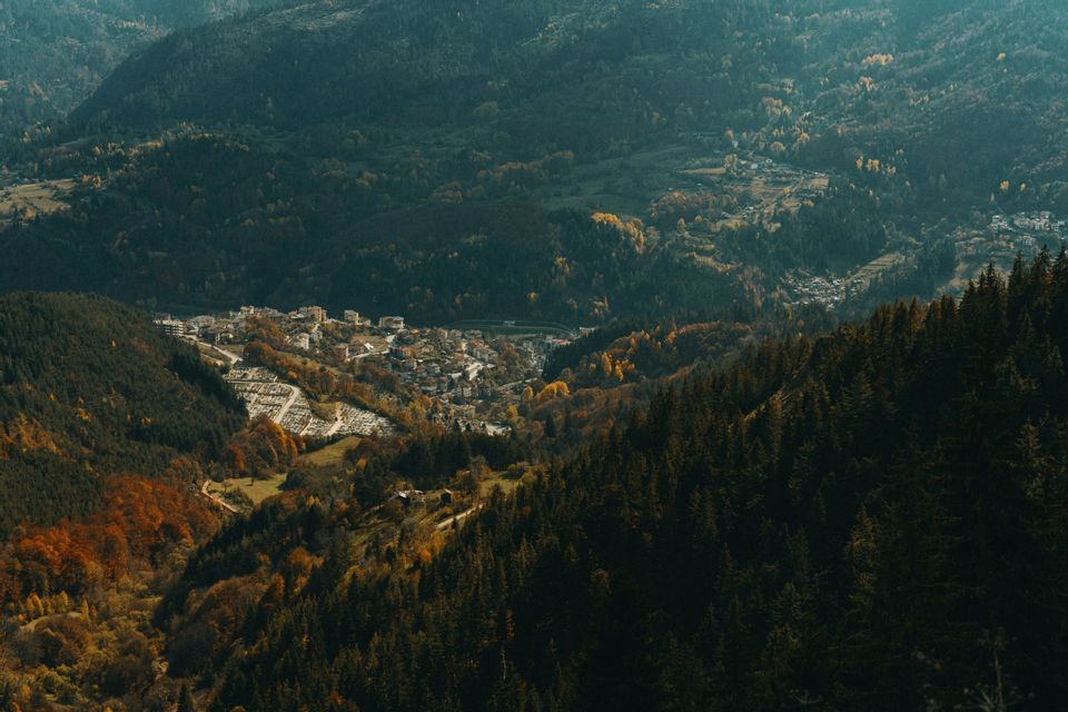 Vue plongeante sur une petite ville nichée dans une vallée montagneuse, entourée de forêts denses aux couleurs automnales.