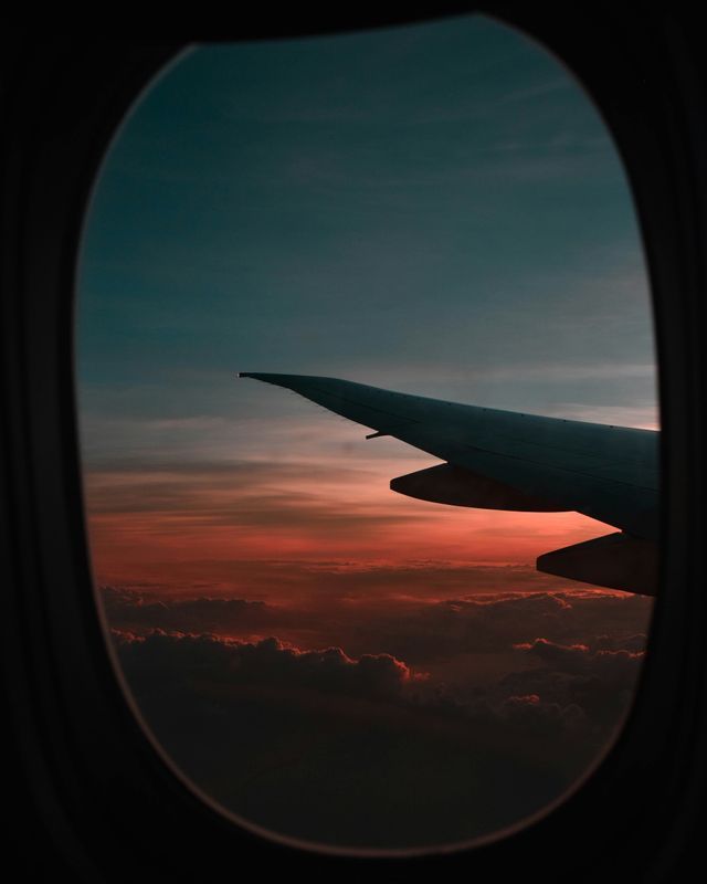 Vue depuis le hublot d'un avion, l'aile survolant les nuages sous un coucher de soleil rouge et orange.