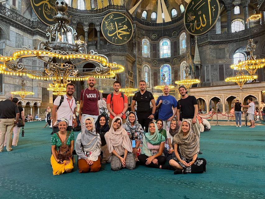 Un gruppo WeRoad posa per una foto su un tappeto verde all'interno di una grande moschea ornata con grandi lampadari.
