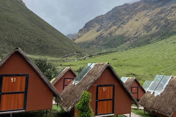 Una hilera de pequeñas cabañas rojizas con techos de paja y claraboyas en un frondoso valle verde de montaña.