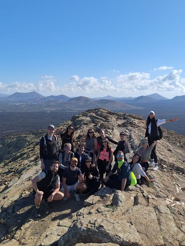 Un viaggio di gruppo WeRoad in posa per una foto su una cresta rocciosa di montagna, con un paesaggio vulcanico sullo sfondo.