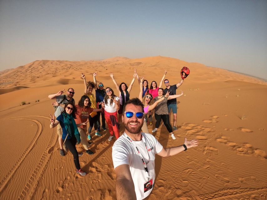 A man takes a selfie with a WeRoad group trip as they pose and smile on large sand dunes in a desert.