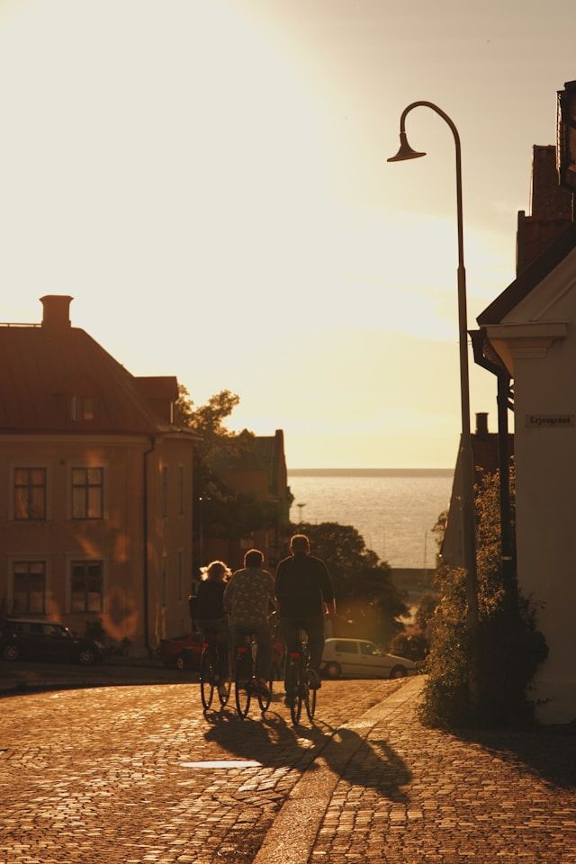 Eine WeRoad-Gruppenreise mit drei Personen, die bei einem warmen Sonnenuntergang eine Kopfsteinpflasterstraße hinunter zum Meer radeln.