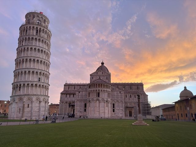 Der Schiefe Turm von Pisa und der Dom von Pisa auf einem grünen Rasen unter einem farbenprächtigen Sonnenuntergangshimmel.