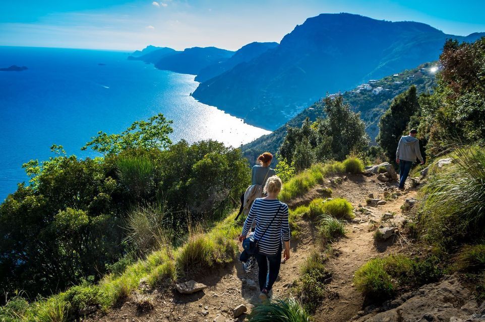 Un viaje en grupo de WeRoad haciendo senderismo por un sendero en un acantilado, con vistas a un mar azul brillante y una costa montañosa.