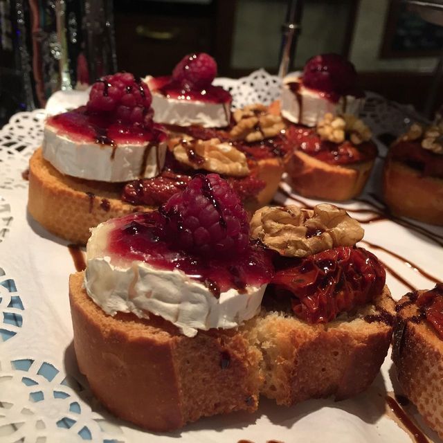 Close-up of crostini topped with goat cheese, raspberries, walnuts, and sun-dried tomatoes, drizzled with balsamic glaze.