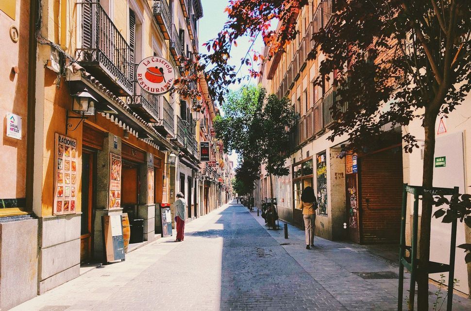 A sunlit view down a narrow cobblestone street lined with tall buildings, with a few people walking on the sidewalk.