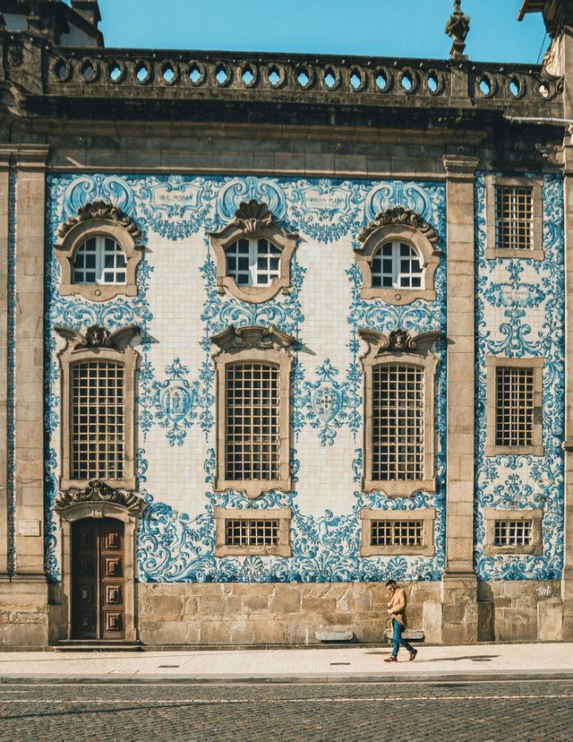 Una persona cammina su un marciapiede davanti a una facciata di un edificio coperta di intricate piastrelle decorative blu e bianche.