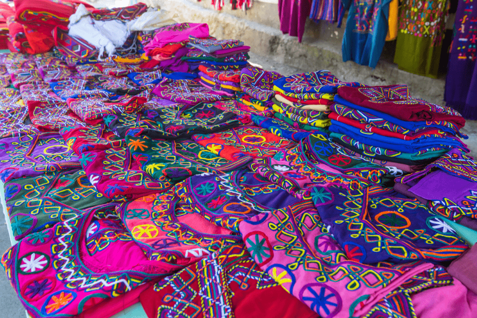 Nahaufnahme von farbenfrohen, aufwendig bestickten Textilien mit geometrischen Mustern, ausgebreitet auf einem Marktstand.