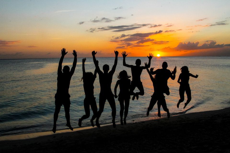 Sagome di un gruppo WeRoad che salta su una spiaggia al tramonto sull'oceano.