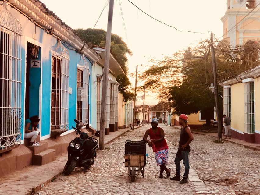 Due uomini parlano su una strada acciottolata fiancheggiata da case coloniali colorate al tramonto.