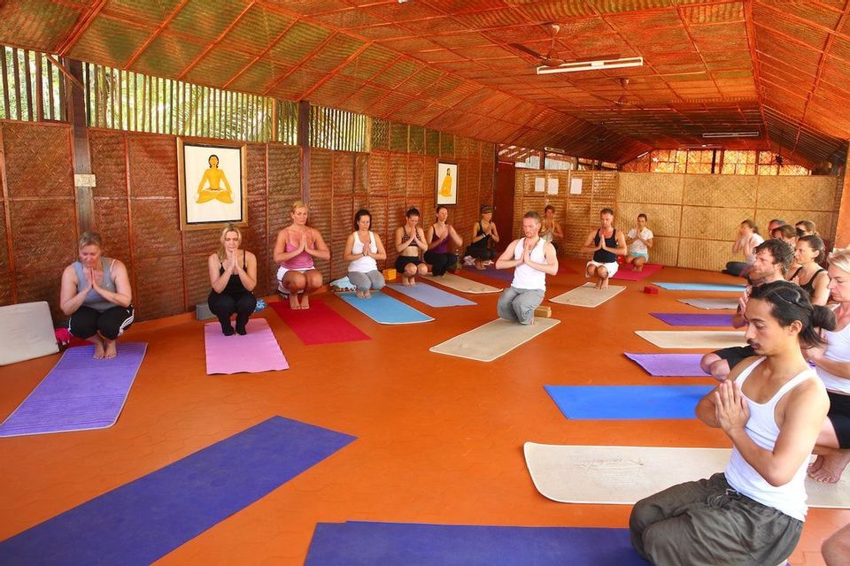 Un gruppo WeRoad partecipa a una lezione di yoga su tappetini colorati in uno studio con pavimento arancione e pareti intrecciate.