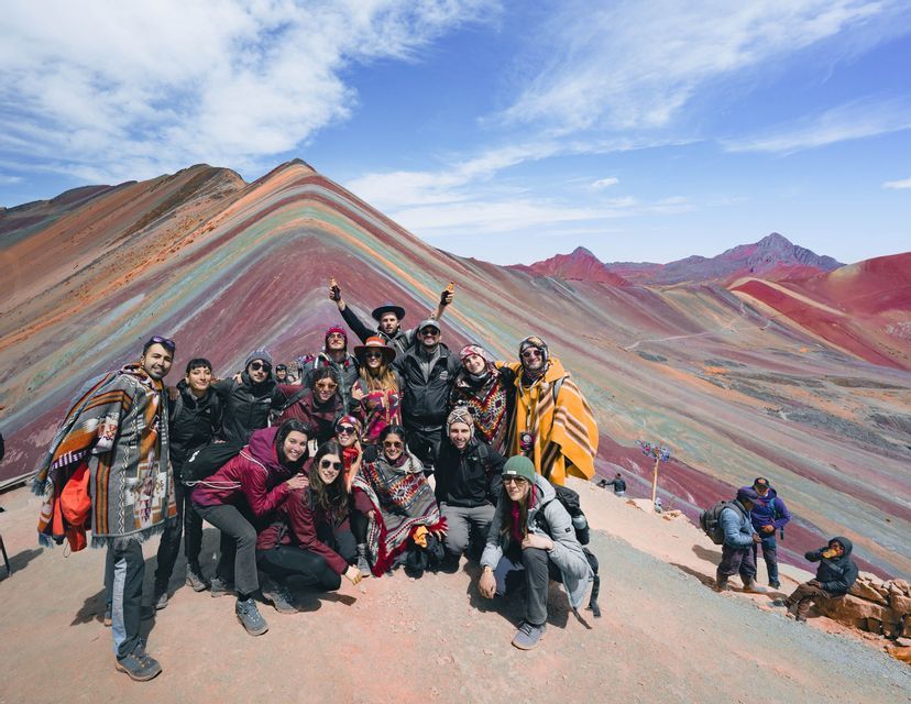 Un grupo de viaje de WeRoad posa para una foto en la ladera de una montaña con una montaña grande, colorida y rayada al fondo bajo un cielo azul.