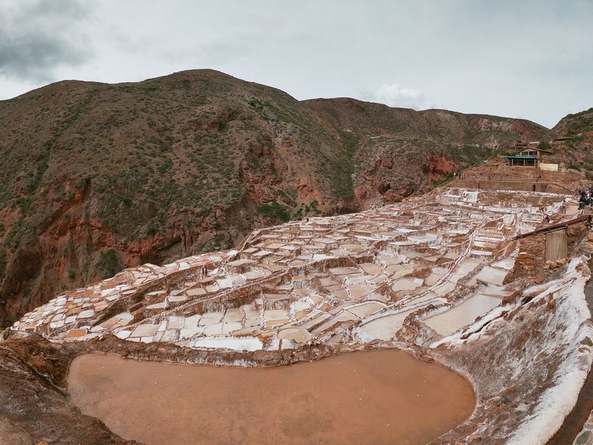 A wide view of white and brown terraced salt pans covering a mountainside under an overcast sky.