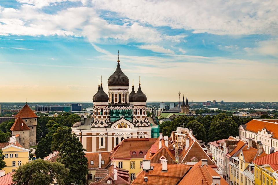 Une cathédrale ornée aux dômes en oignon noirs domine les toits de tuiles rouges d'une ville historique sous un ciel bleu nuageux.