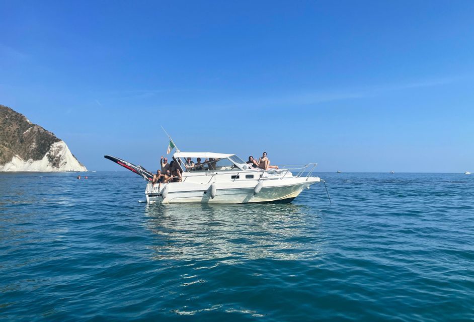 Un viaggio di gruppo WeRoad in relax su un motoscafo bianco in mare, con una scogliera sullo sfondo sotto un cielo azzurro.