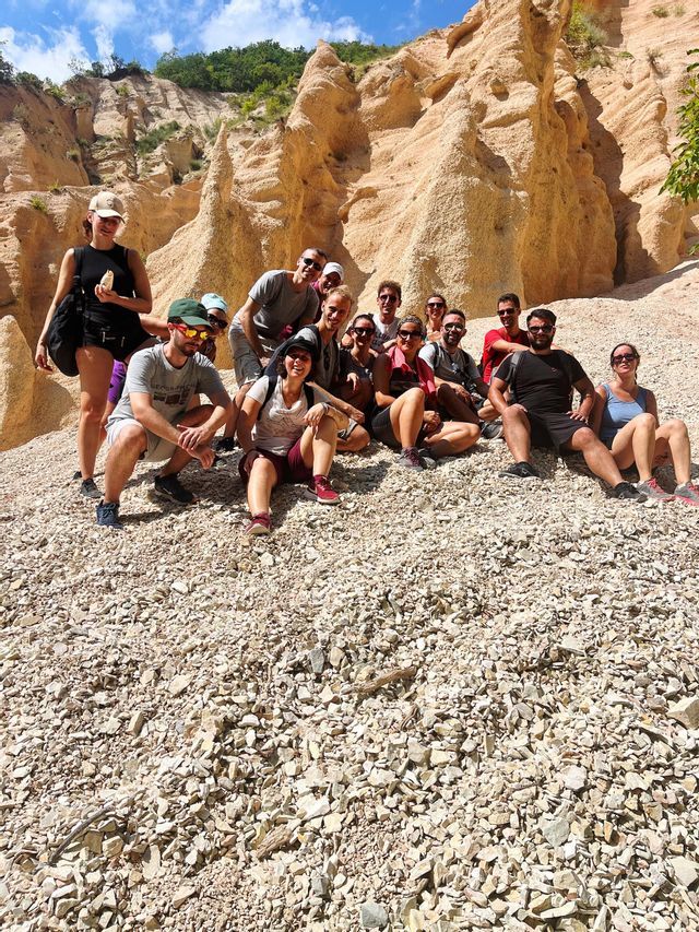 Un viaggio di gruppo WeRoad in posa per una foto su un pendio ghiaioso, con grandi formazioni rocciose erose sullo sfondo sotto un cielo blu.