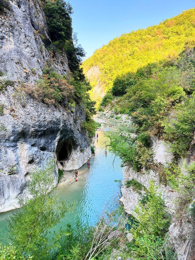 Un gruppo WeRoad fa il bagno in un fiume turchese in fondo a un canyon ripido e roccioso con colline verdi e boscose.