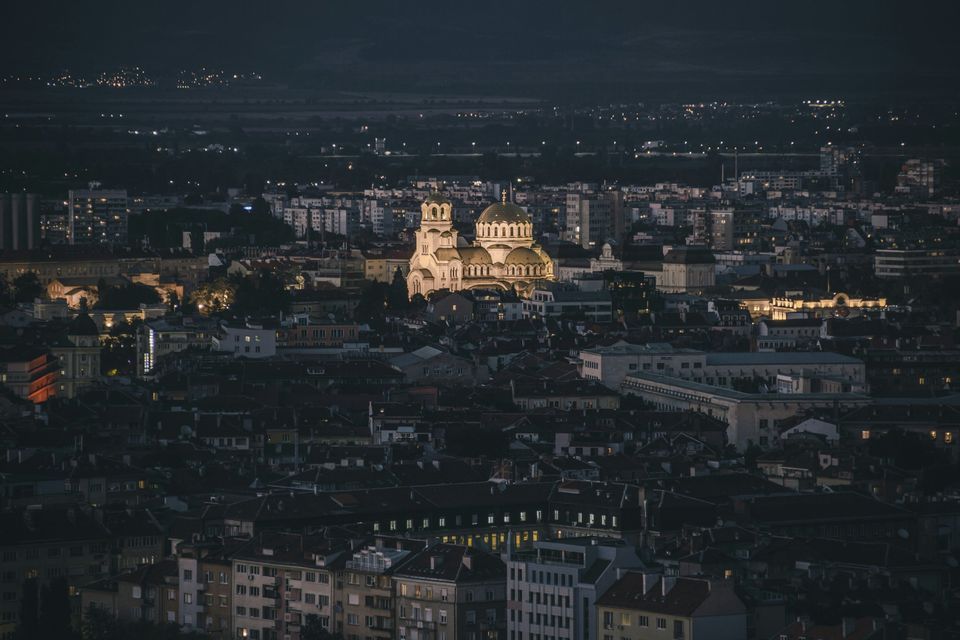 Una catedral iluminada con cúpulas doradas se erige en el centro de un extenso paisaje urbano nocturno.