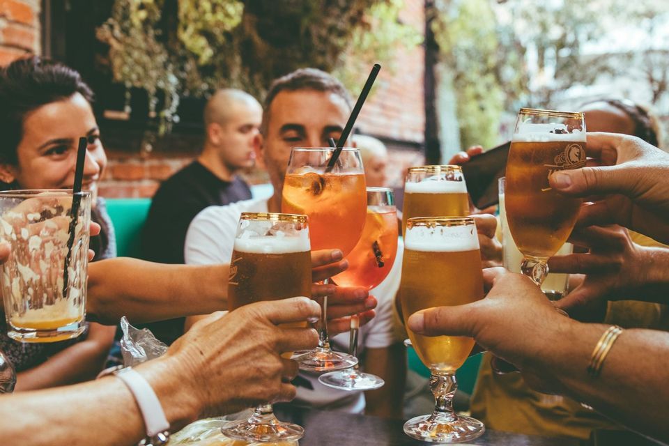 Un viaggio di gruppo WeRoad di persone che brindano con bicchieri di birra e cocktail attorno a un tavolo all'aperto.