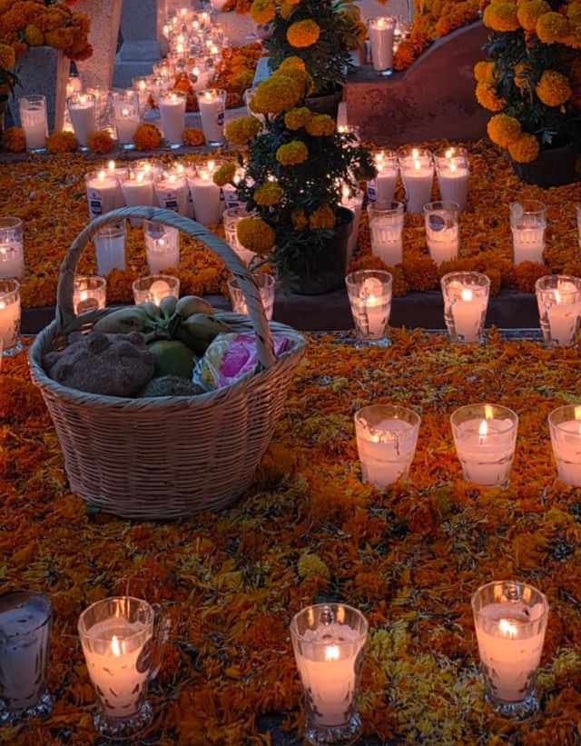 Un'ofrenda del Giorno dei Morti con candele accese in portacandele di vetro, petali di calendula arancioni e un cestino di pane.