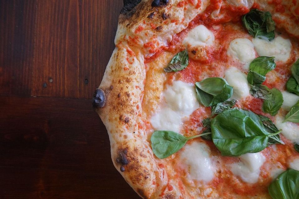 Un primo piano di una pizza Margherita napoletana con basilico fresco e mozzarella su un tavolo di legno scuro.