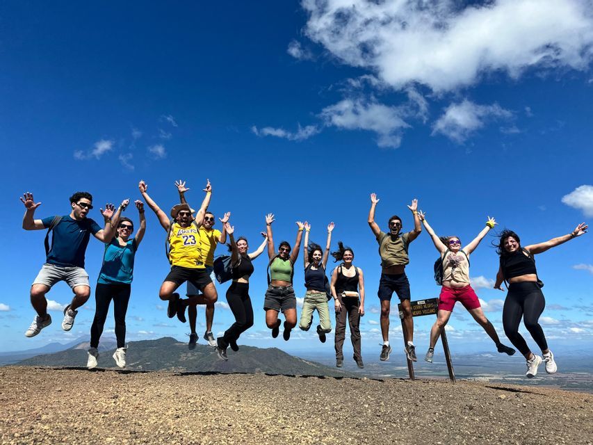 Un voyage en groupe WeRoad de onze personnes sautant à l'unisson au sommet d'une montagne sous un ciel bleu vif parsemé de nuages.