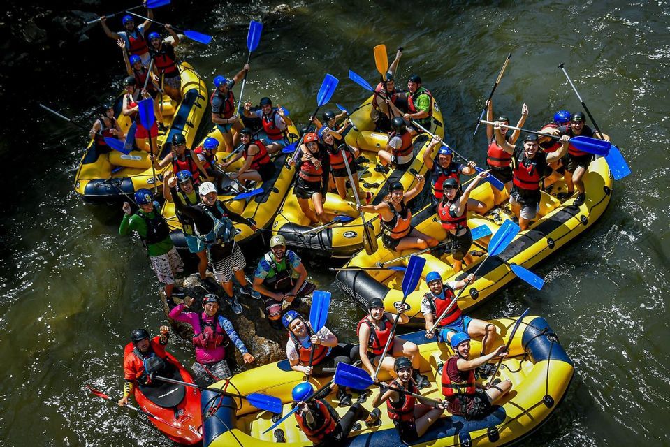 Vista aerea di un gruppo WeRoad in viaggio che posa su diverse zattere gialle su un fiume, con le pagaie alzate in aria.