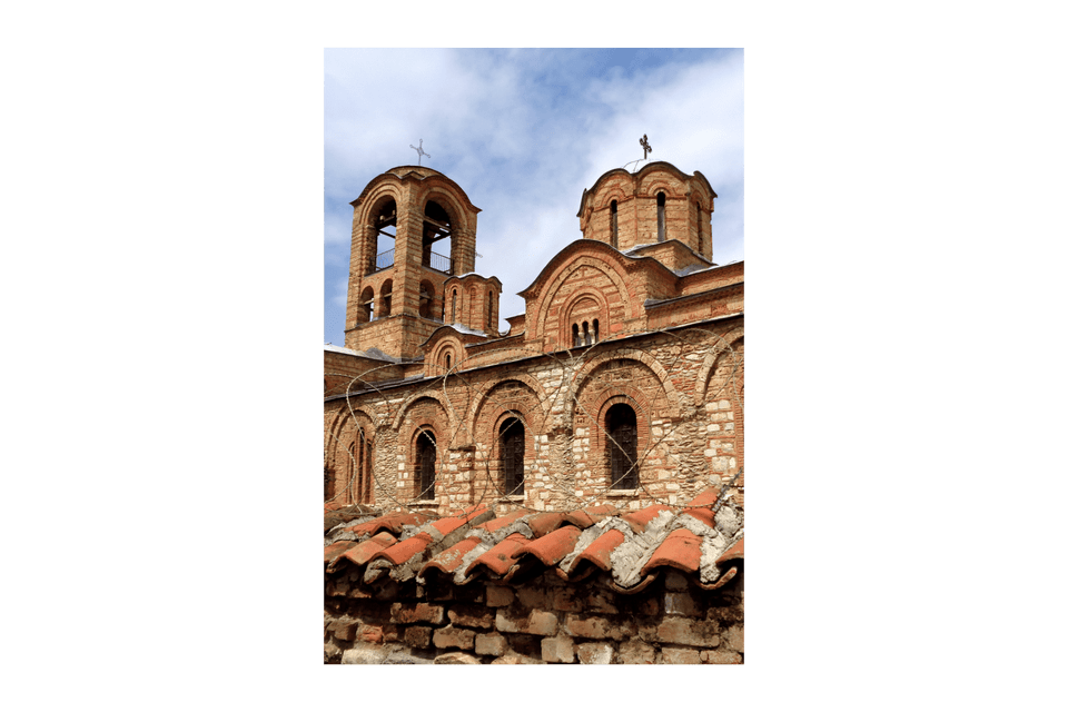 Una vecchia chiesa costruita in pietra e mattoni, con un campanile e cupole sotto un cielo azzurro nuvoloso.