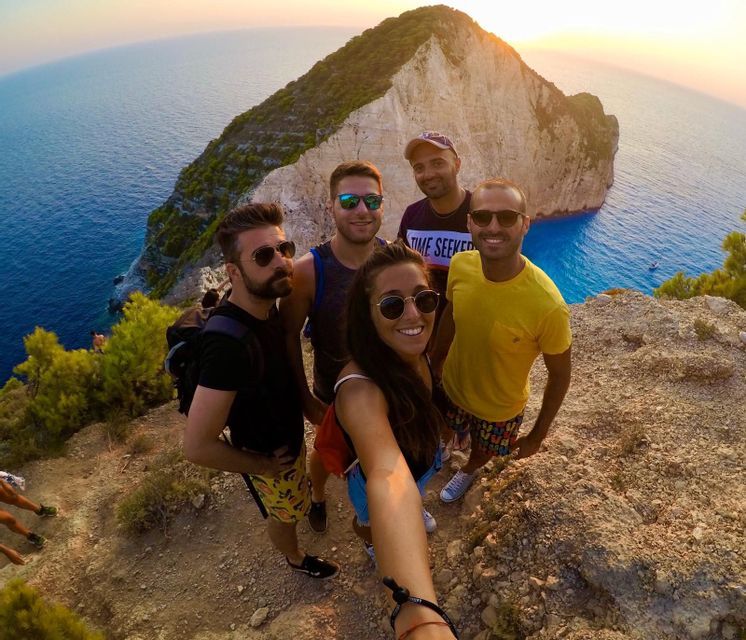 Un gruppo WeRoad si scatta un selfie su una scogliera a picco sul mare e una grande formazione rocciosa al tramonto.