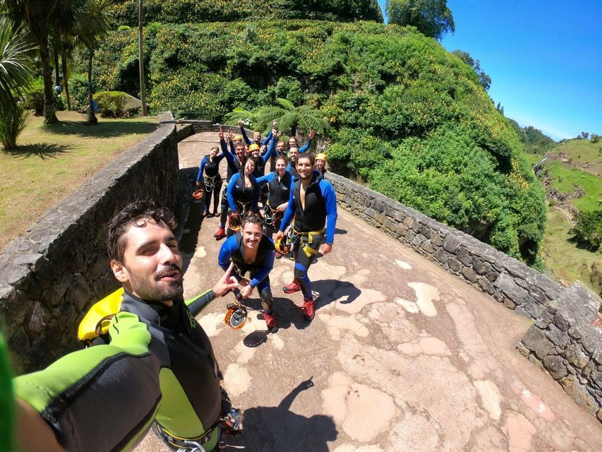 Un gruppo WeRoad in muta e imbracatura si scatta un selfie su un ponte di pietra immerso in rigogliose colline verdi.